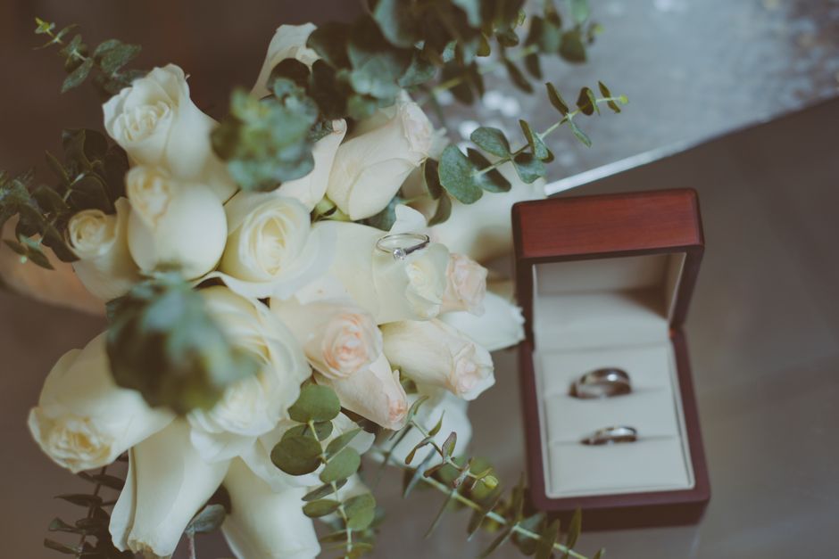 A close-up of a bouquet consisting of white roses and green eucalyptus leaves, arranged on a surface with soft natural lighting highlighting the delicate petals and textured foliage. Beside the bouque