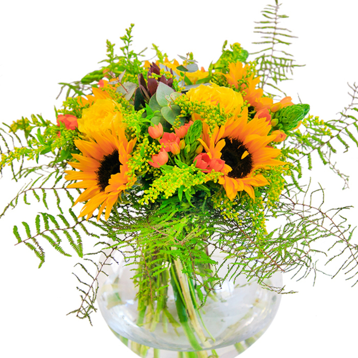 This brilliant bouquet captures the exuberance of Harefield's lush landscapes, where sunflowers and yellow garden roses bloom in tandem throughout the season. The golden flowers are nestled together, their faces alive with energy against stately dark centers. Spirals of yellow roses add plush volume and regal grace, while scarlet clusters of Hypericum berries shimmer between the blooms-colourful punctuation marks on a canvas of unfolding greens. Lively greenery abounds, with feathery fern tendrils, slender filler spikes possibly of goldenrod, and delicate pale yellow sprigs evoking Harefield's wild verges and parklands. Blueish eucalyptus leaves lend rustic contrast and a subtle, herbal aroma redolent of a walk through the neighbouring countryside. The clear, round vase, full of shimmering water, displays every fresh stem in elegant order and brings a polished note to the rustic arrangement. Perfect as a birthday surprise, anniversary gesture, or cheerful centrepiece, this arrangement brings the spirit of Harefield's open spaces and friendly village atmosphere into any home.