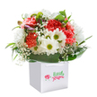 This uplifting bouquet, gracefully presented in a modern white gift bag, seems to capture the gentle spirit of Harefield-its village greens, riverbanks, and welcoming homes. At the heart of the design, vibrant coral, peach, and rosy red carnations burst with ruffled textures, their petals soft as afternoon sunlight filtering through the trees by Harefield Hospital. Cheerful white daisies, each with a tiny yellow-green heart, weave among the carnations, brightening the arrangement like laughter on a summer's walk near Marlborough Hill. Baby's breath is scattered throughout, its fine white florets adding gentle charm and softness, reminiscent of warm, breezy days. Sprinkled quietly along the left, a handful of purple-edged buds bring a sense of promise and subtle depth, completing the symphony of colour and shape. Wrapped by a collar of deep, glossy green foliage, the flowers are gathered into a lush round composition that suggests care and heartfelt intention. The sturdy gift bag, fitted with neat ribbon handles, ensures that this thoughtful bouquet can be delivered with ease throughout Harefield-ready to celebrate birthdays, anniversaries, or milestones with local friends and family. Bathed in clean, white light, every petal and leaf comes to life, highlighting freshness and the loving effort poured into each arrangement by Harefield's talented florists. It's a stunning expression of joy, gratitude, and the timeless beauty found around Harefield.